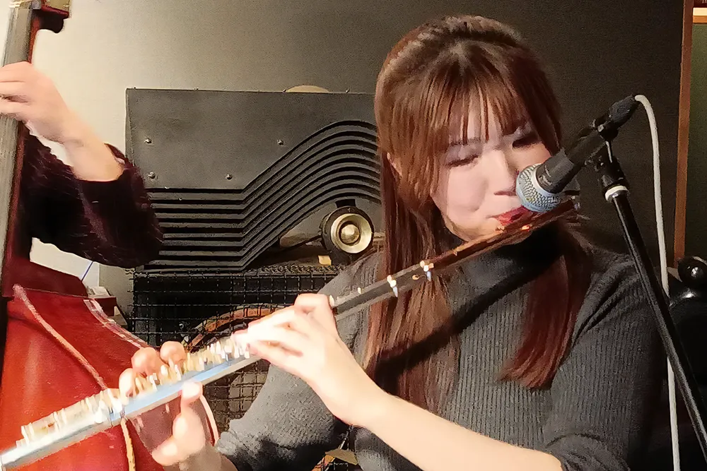 シックなライブ会場でフルートを吹く永田梨紗の写真