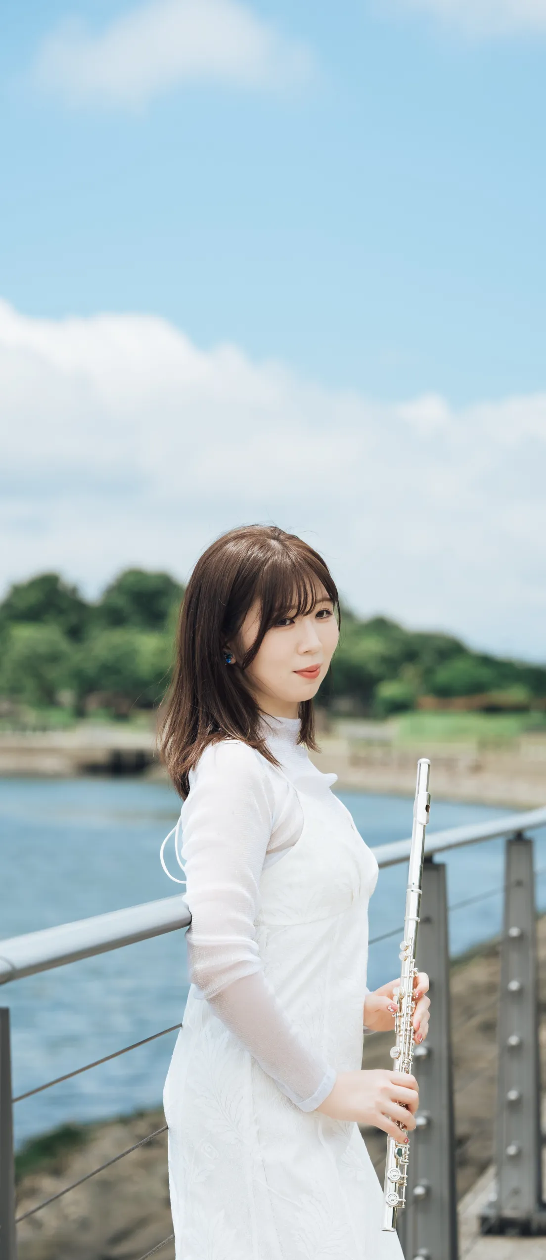 青空と海を背景に永田梨紗がフルートを持って爽やかな表情で立っている写真